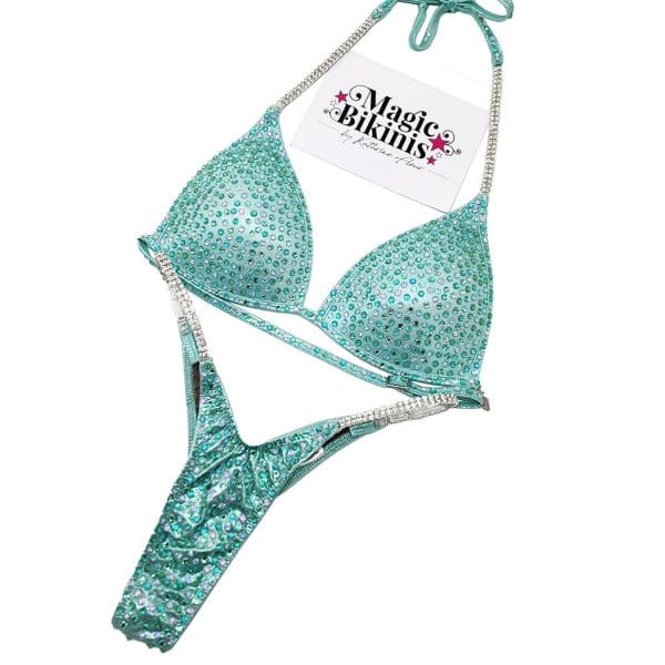 Competition Bikini No.205 – Striking Light Teal Mystique bikini adorned with a stunning mix of Teal and Clear crystals. Designed for a flawless fit, ultimate sparkle, and a standout stage presence.